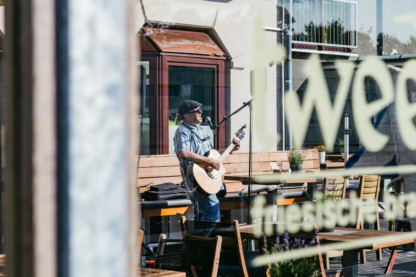Live-Musiker auf der Terrasse, durch das Schaufenster mit tween-Schriftzug gesehen