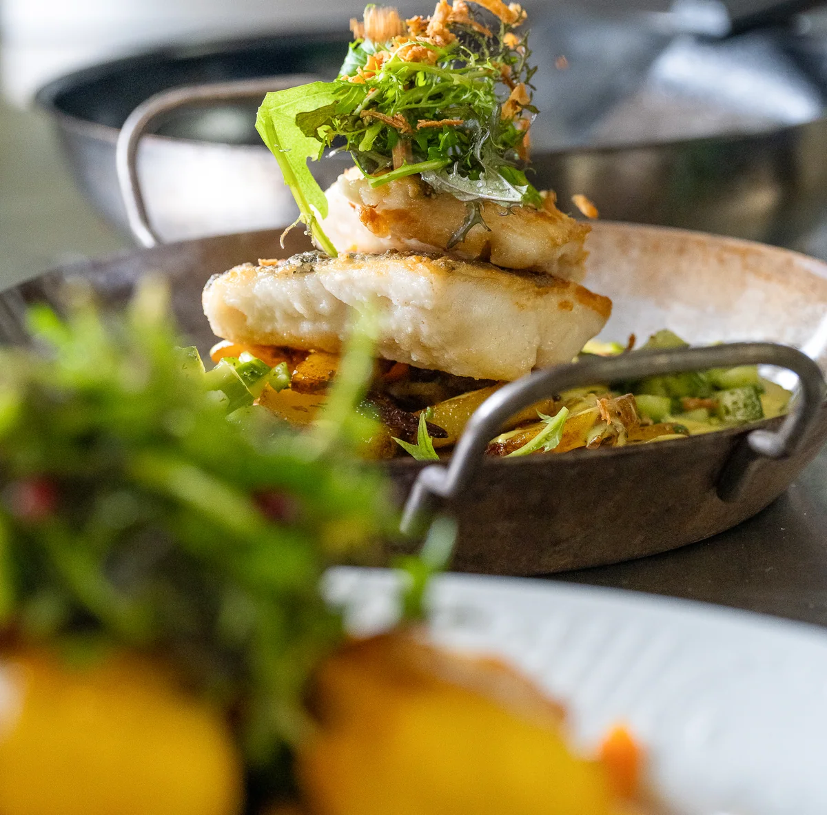Gebratener Pannfisch mit Röstzwiebeln und Rucola in der Pfanne, dazu Bratkartoffeln